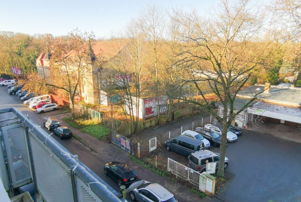 Overhead view of a street and parking lot with cars, bare trees, and graffiti-covered walls in sunlight.