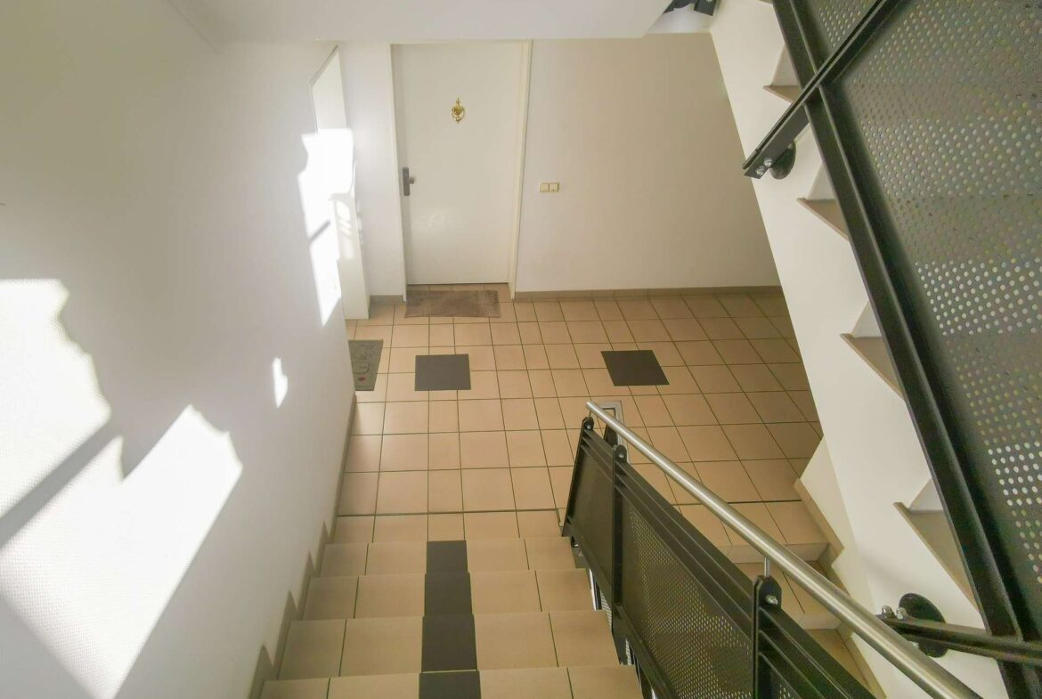 Interior stairwell with beige floor tiles, metal railing on the right, and a closed door at the top landing.