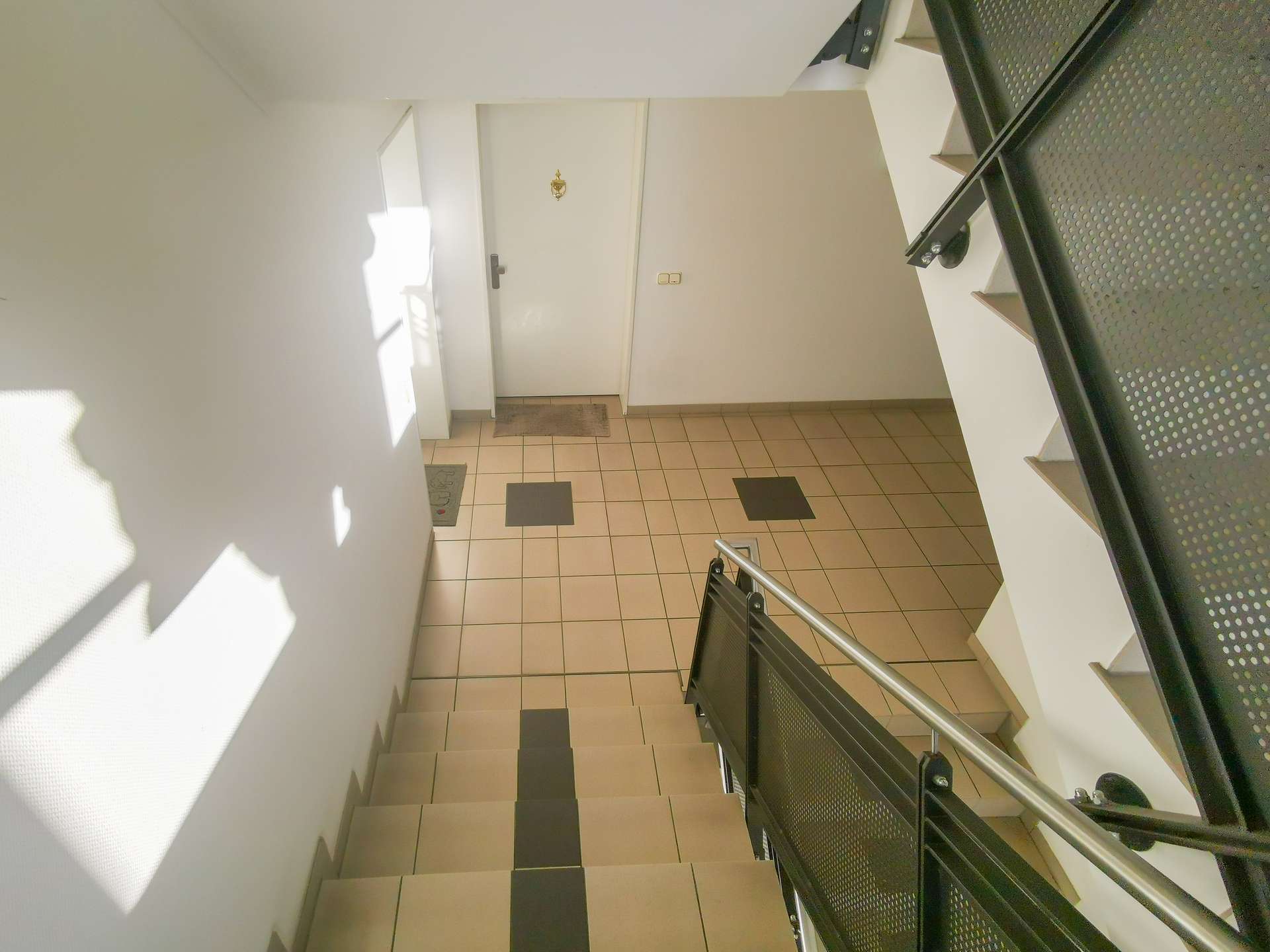 Interior stairwell with beige floor tiles, metal railing on the right, and a closed door at the top landing.
