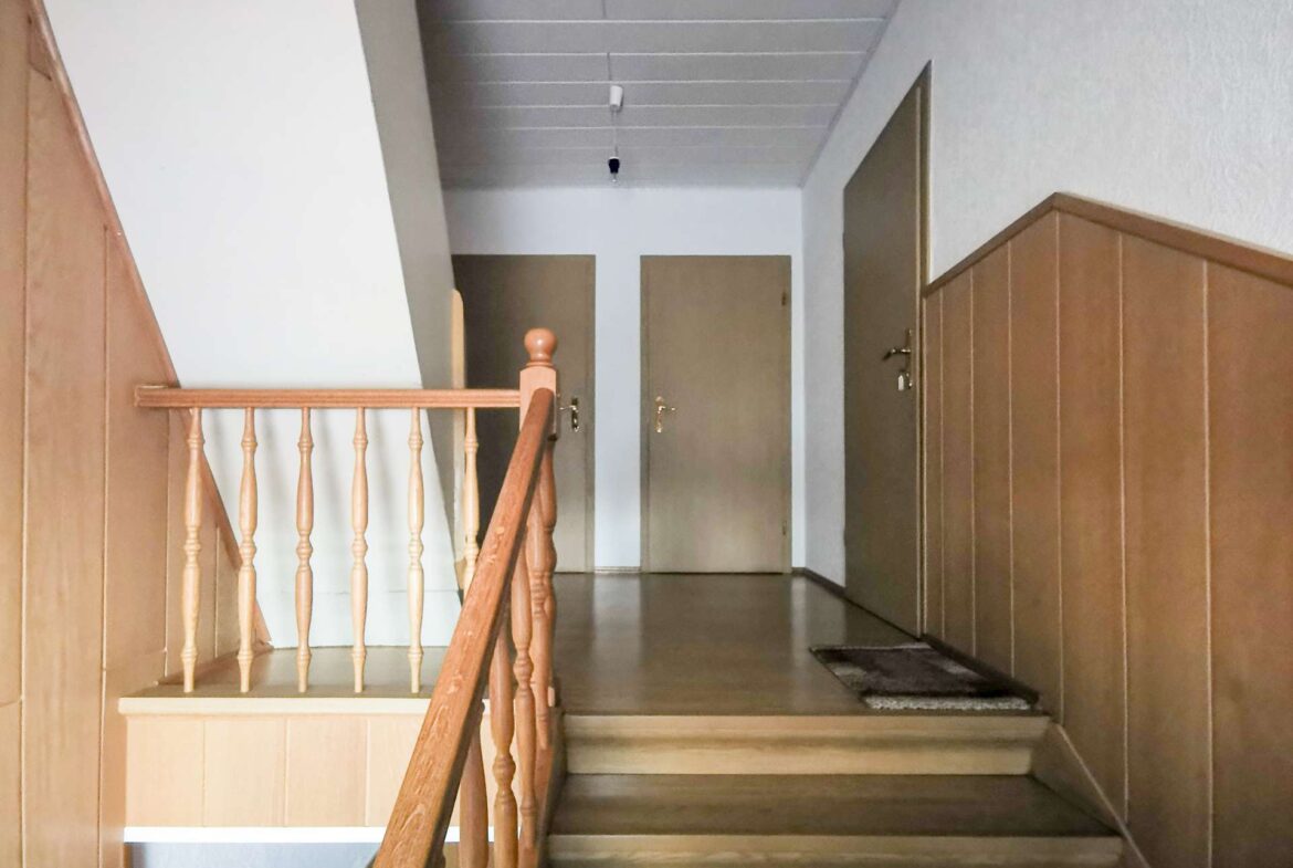 Indoor stairwell with a wooden banister and paneling, leading to a hallway with two closed doors at the end.