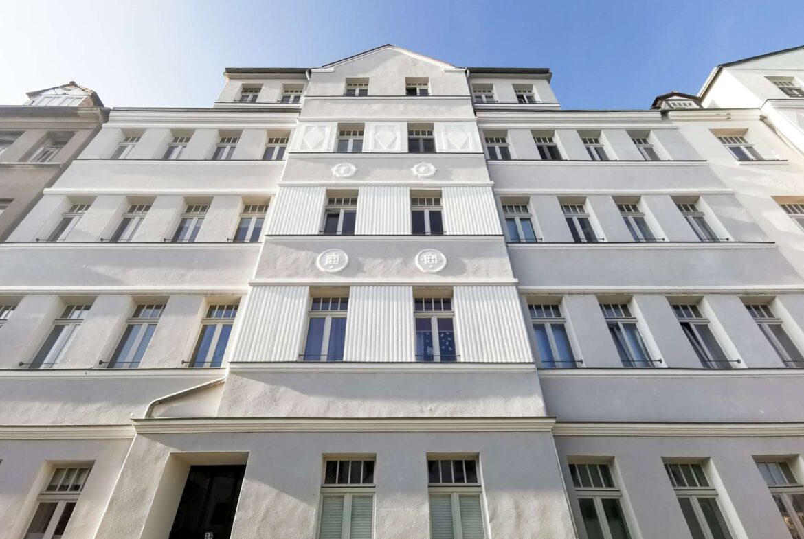 Upward-looking view of a white residential building with vertical fluted columns and decorative motifs on the façade against a clear blue sky.