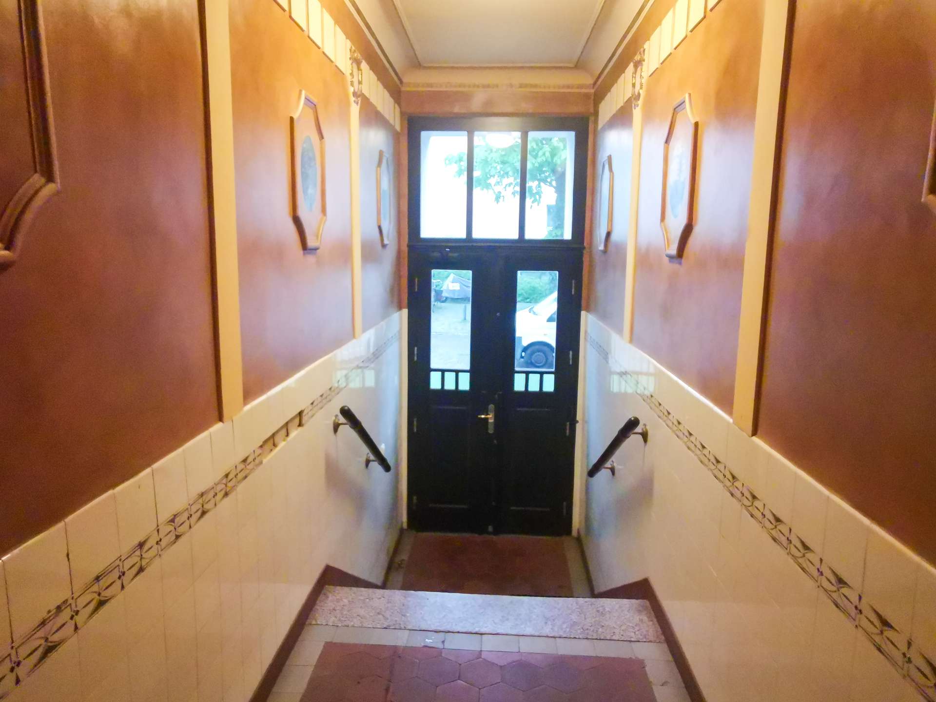 Narrow tiled stairwell with brown walls, leading to a black door with glass panels at the end.
