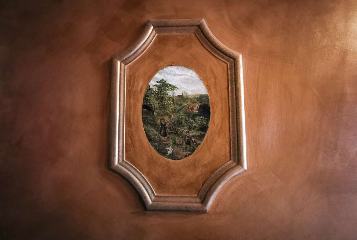 Wooden panel with an oval landscape painting framed in a decorative octagonal inset.