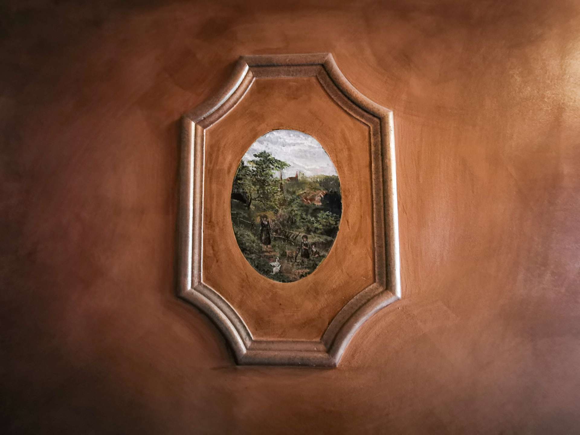 Wooden panel with an oval landscape painting framed in a decorative octagonal inset.