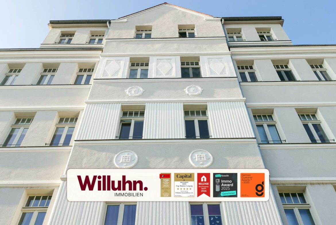 White multi-story building facade with a large Willuhn Immobilien sign and award stickers at street level under a blue sky.
