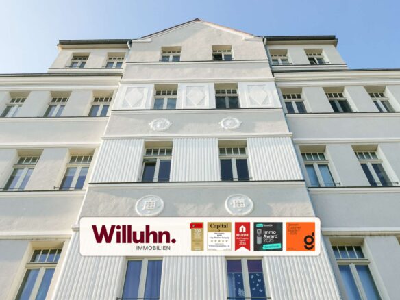 White multi-story building facade with a large Willuhn Immobilien sign and award stickers at street level under a blue sky.