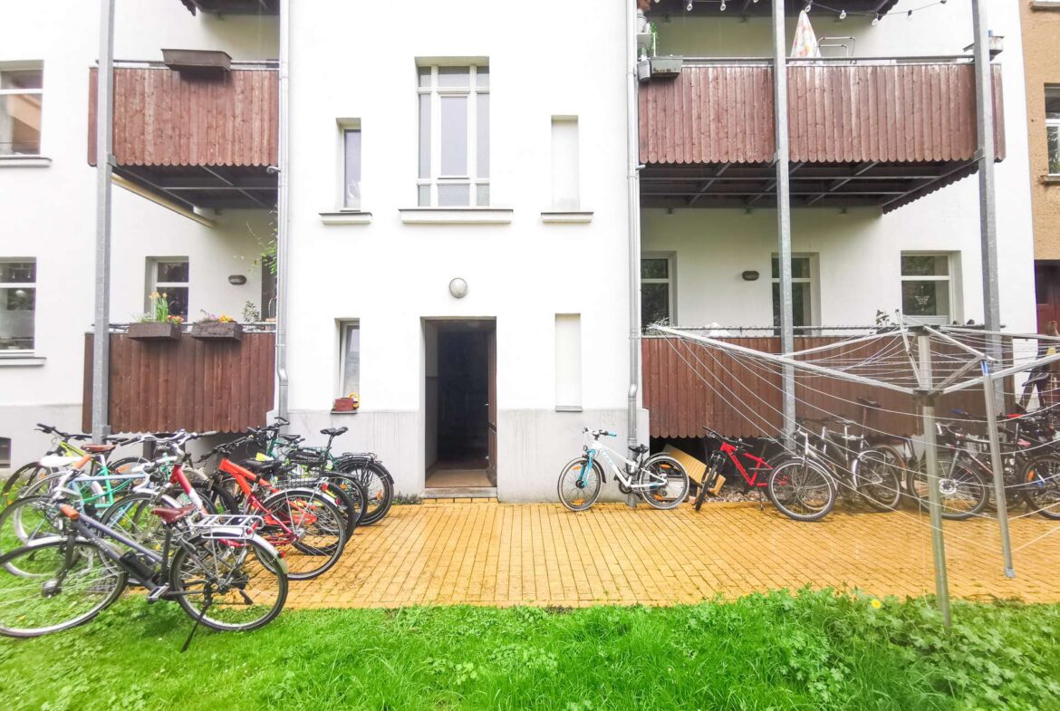 Apartment building courtyard with multiple bicycles parked along the ground-floor balconies and a bright green lawn in foreground