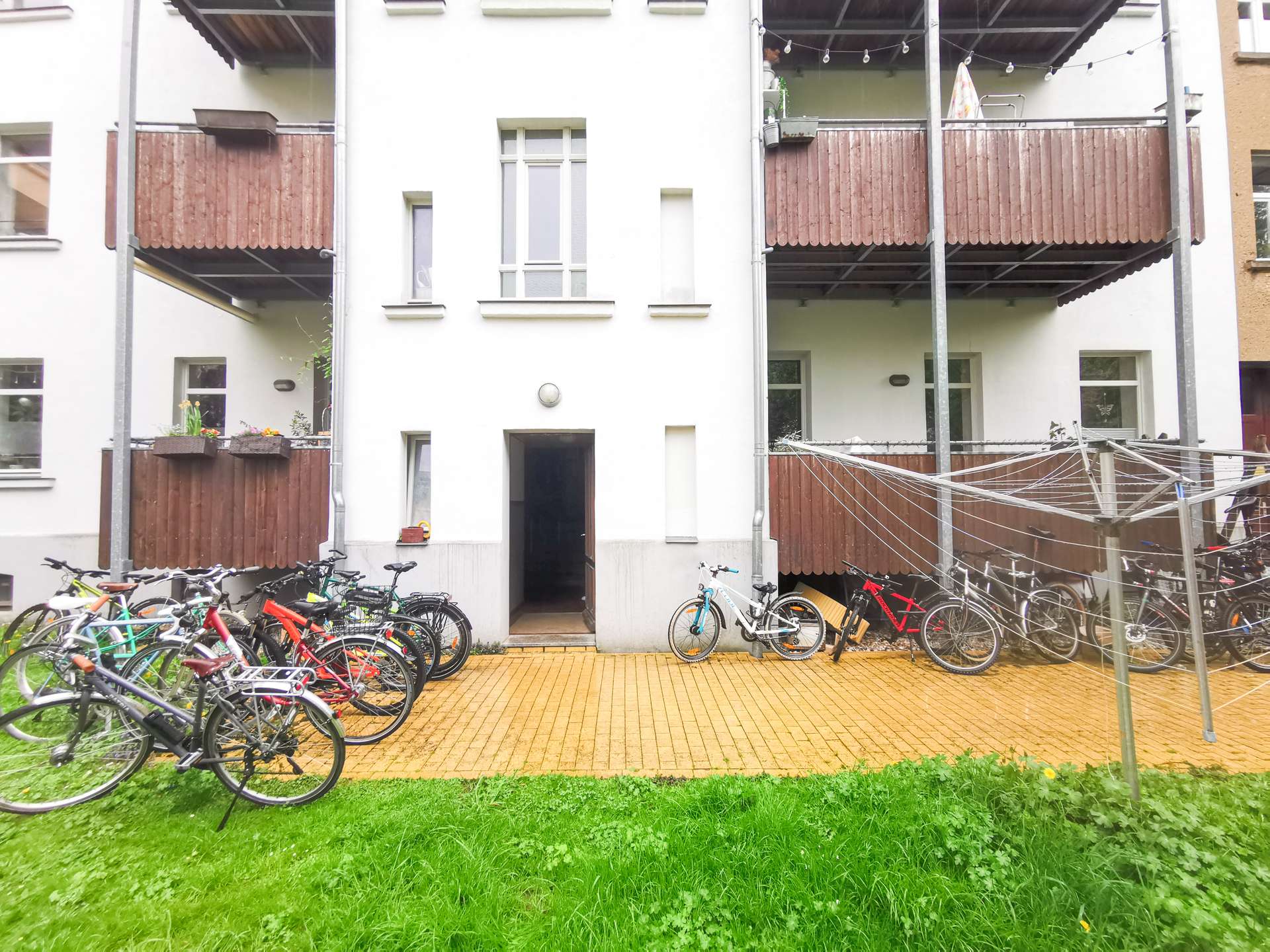 Apartment building courtyard with multiple bicycles parked along the ground-floor balconies and a bright green lawn in foreground