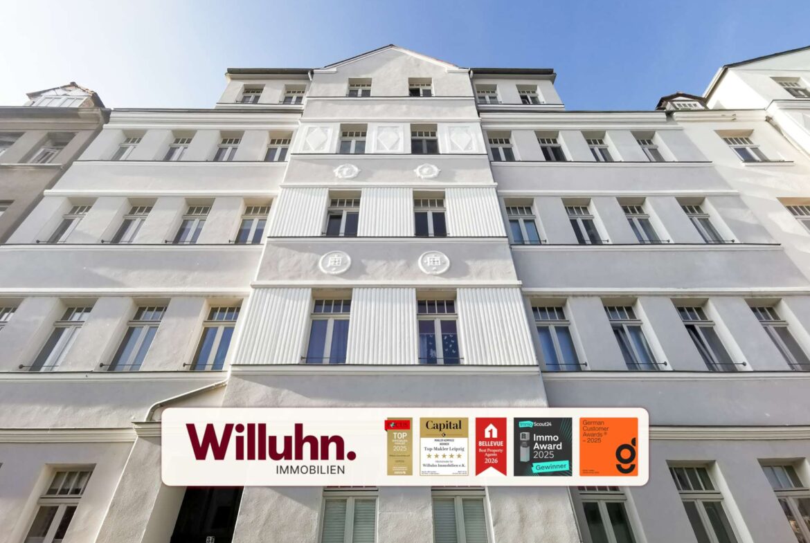 White, multi-story building with a large Willuhn Immobilien sign and award plaques along the street level façade.