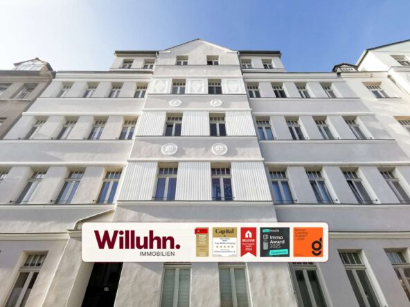 White, multi-story building with a large Willuhn Immobilien sign and award plaques along the street level façade.
