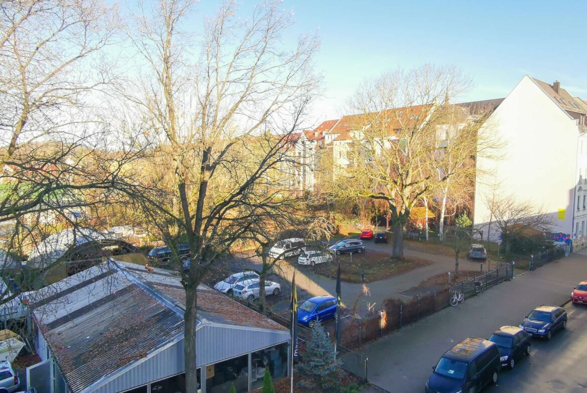 Aerial view of a residential street in winter: bare trees, parked cars along both sides, and row houses with red-tiled roofs under a clear blue sky.