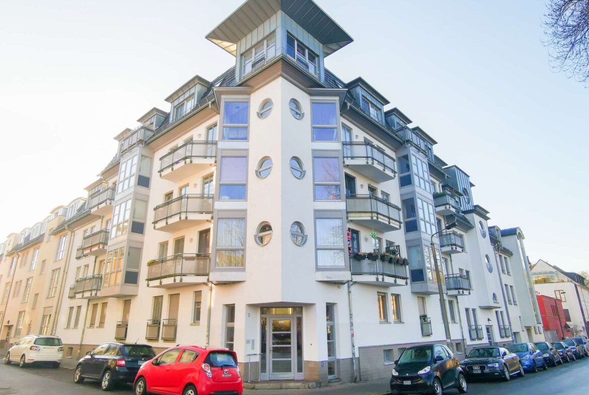 Modern white residential building with rounded windows and balconies on a city street, corner view.