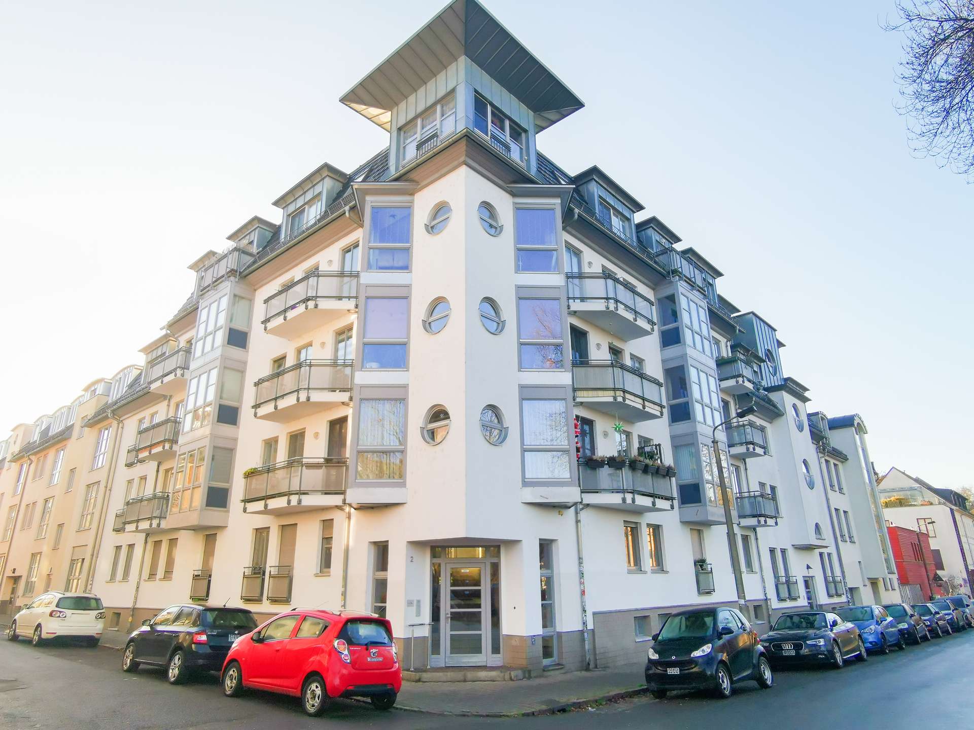 Modern white residential building with rounded windows and balconies on a city street, corner view.
