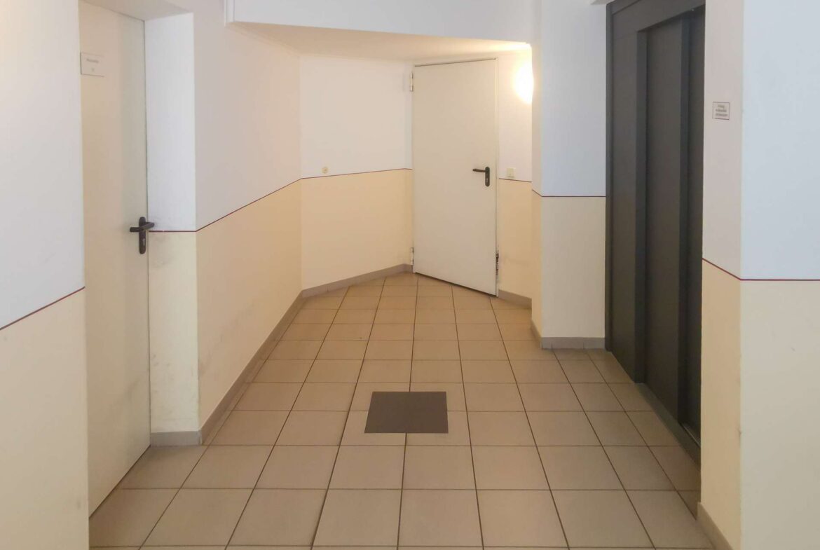 Interior corridor with beige lower walls, white upper walls, and a closed white door at the end; elevator doors on the right; tiled floor