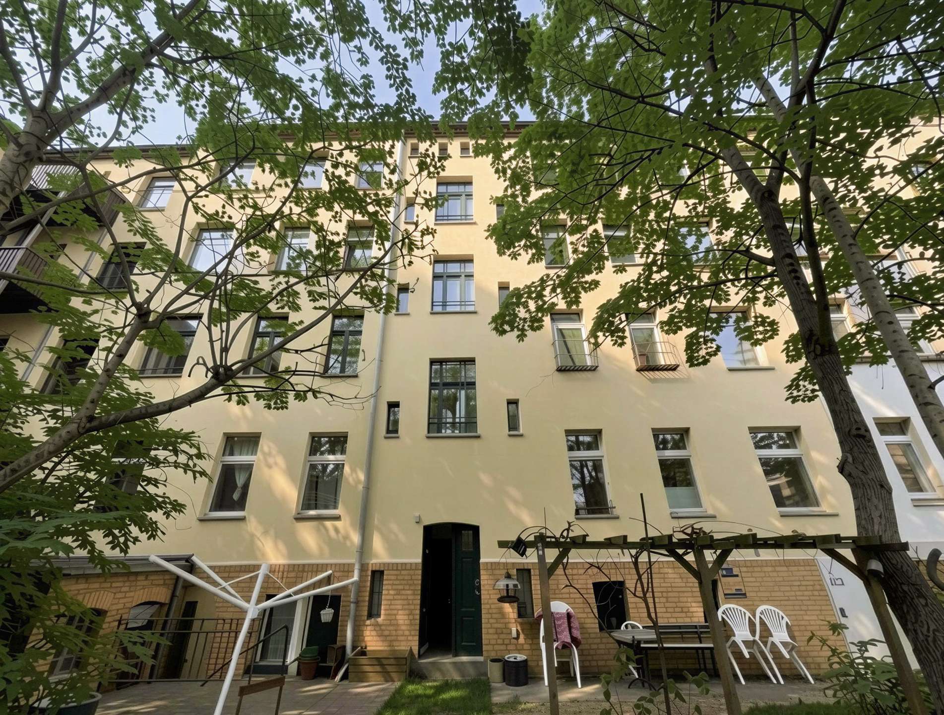 Beige apartment building viewed from a courtyard, with green trees framing the scene.