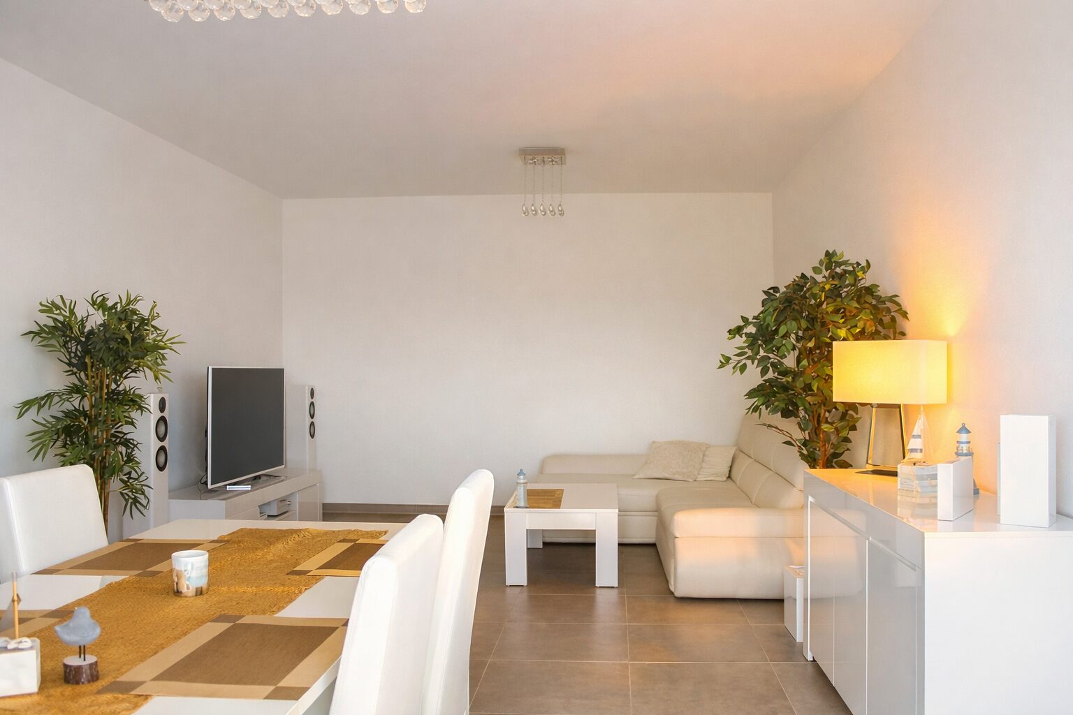 Open-concept living and dining room with white furniture, beige sofa, and tall green plants; bright and modern. (informative)