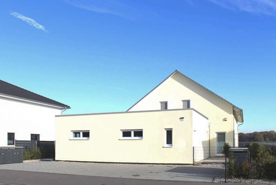 Modern beige house with flat wall and small horizontal windows on a suburban street under a clear blue sky