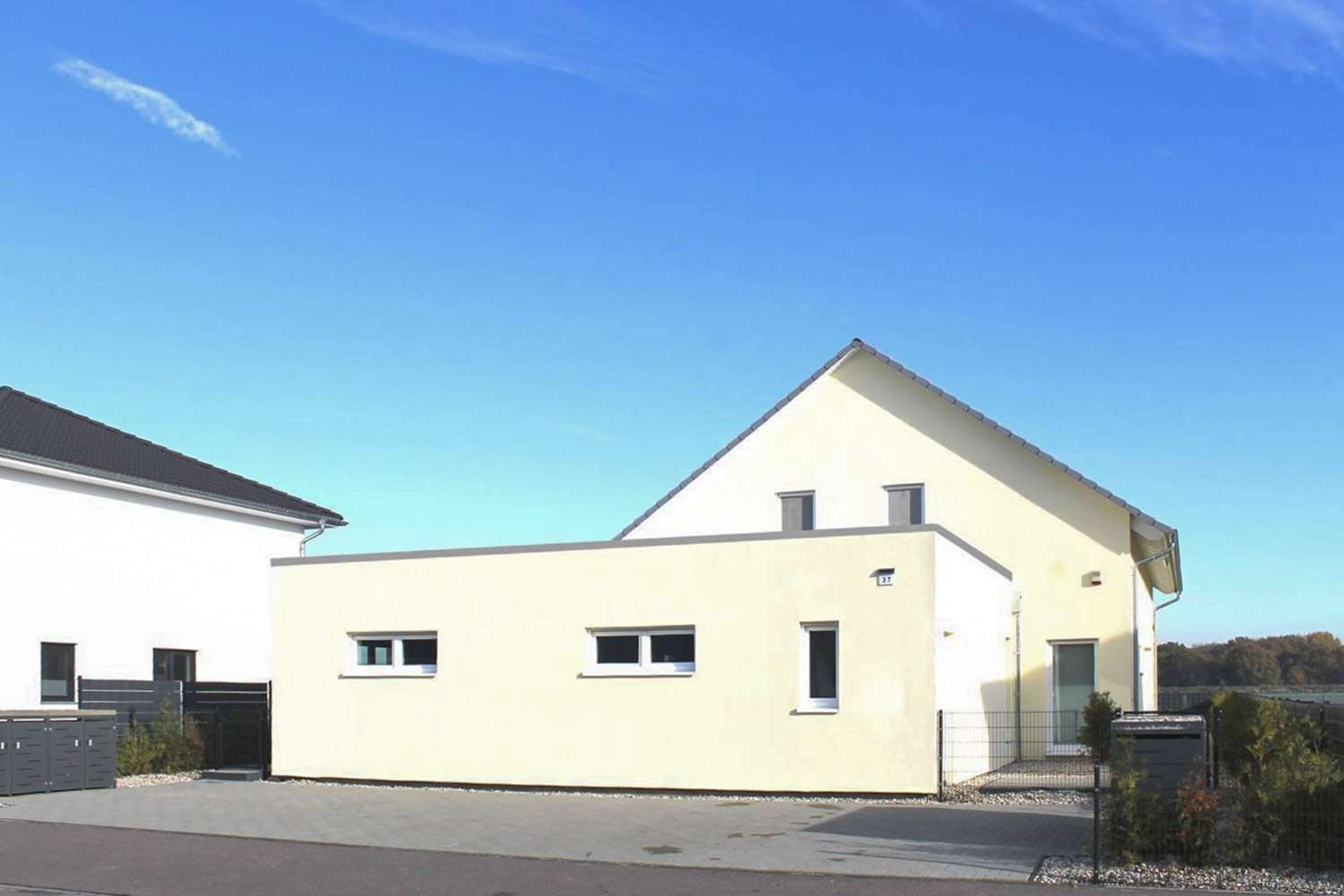 Modern beige house with flat wall and small horizontal windows on a suburban street under a clear blue sky