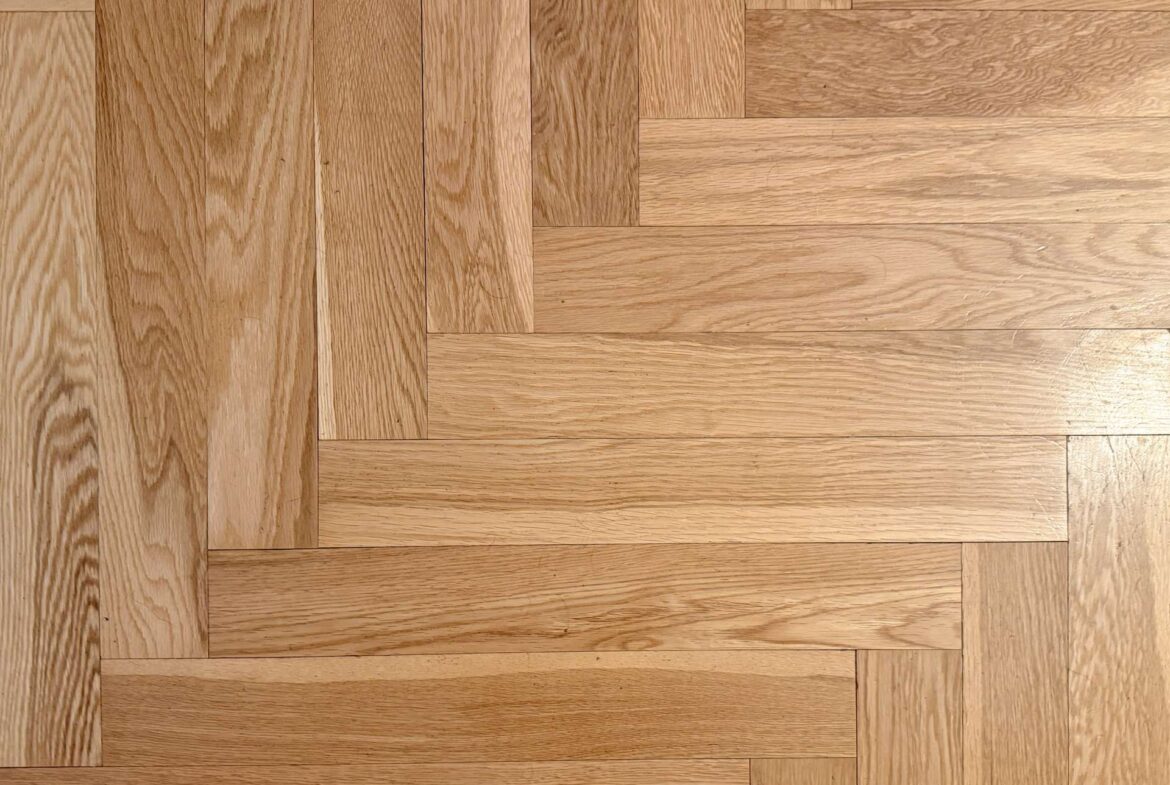 Light oak parquet floor arranged in a herringbone pattern, showing rectangular wooden planks.