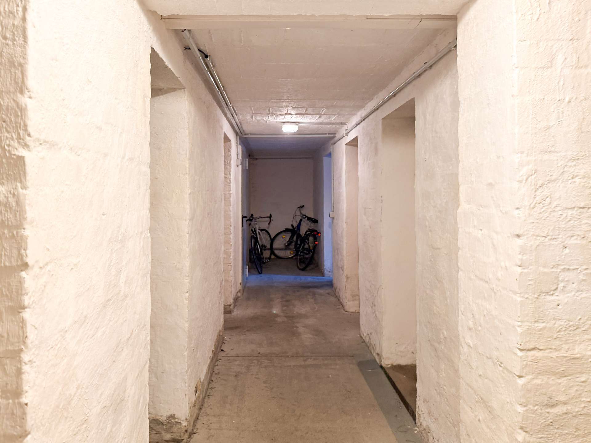 Long concrete basement hallway with white walls; two bicycles parked at the far end.