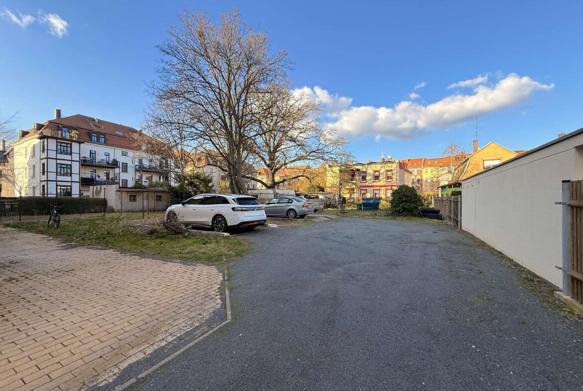 Residential parking lot with several cars, a large leafless tree, and apartment buildings under a blue sky in a quiet neighborhood