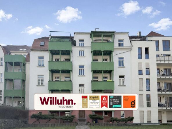 Residential building with green balconies and a large Willuhn Immobilien banner in front.
