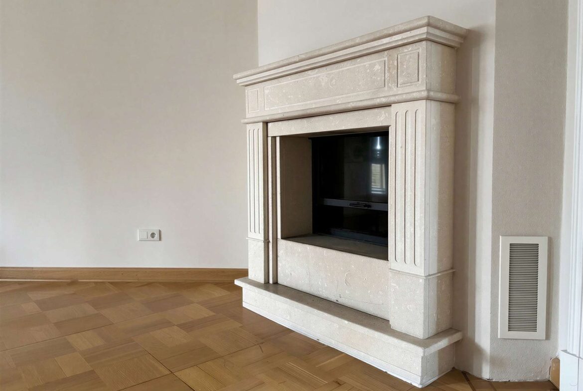 Beige marble fireplace with a decorative mantel in a minimal living room, wood parquet flooring visible.