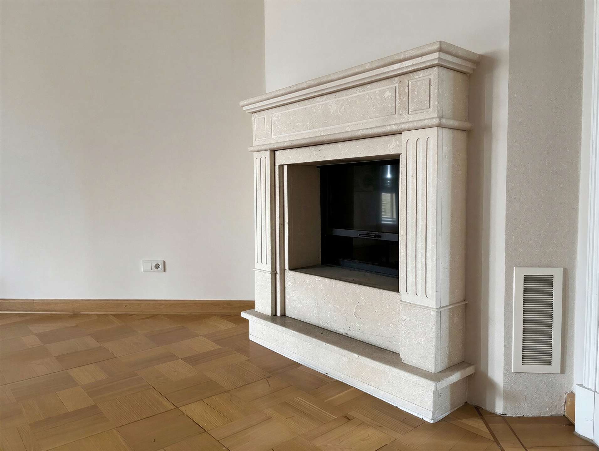 Beige marble fireplace with a decorative mantel in a minimal living room, wood parquet flooring visible.