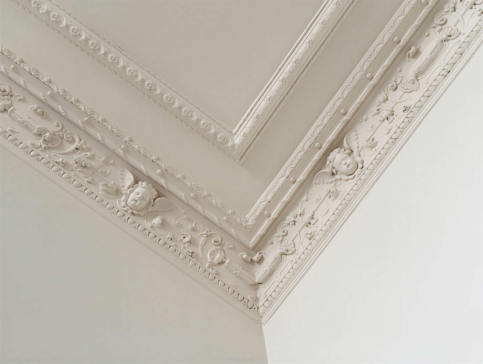 Ornate white plaster molding along a ceiling corner with floral scrolls and cherub faces.
