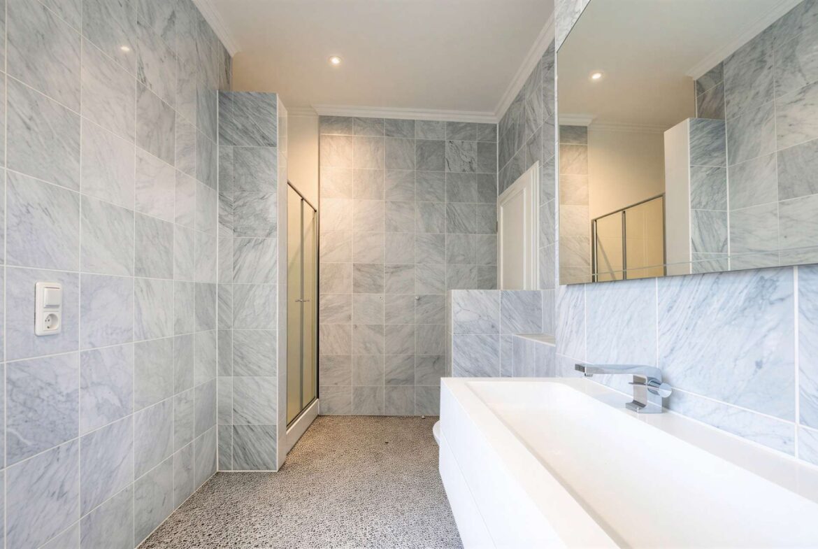 Modern bathroom with gray marble-tiled walls, a white rectangular sink, and a glass shower enclosure.