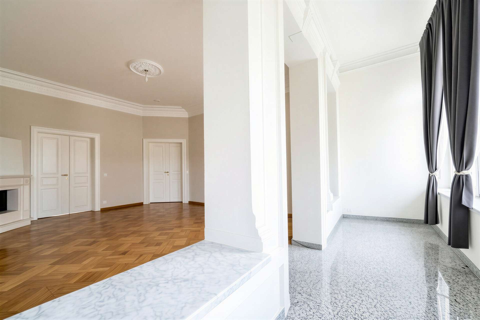 Spacious interior: left room with parquet floor and white doors; right, bright space with grey curtains.