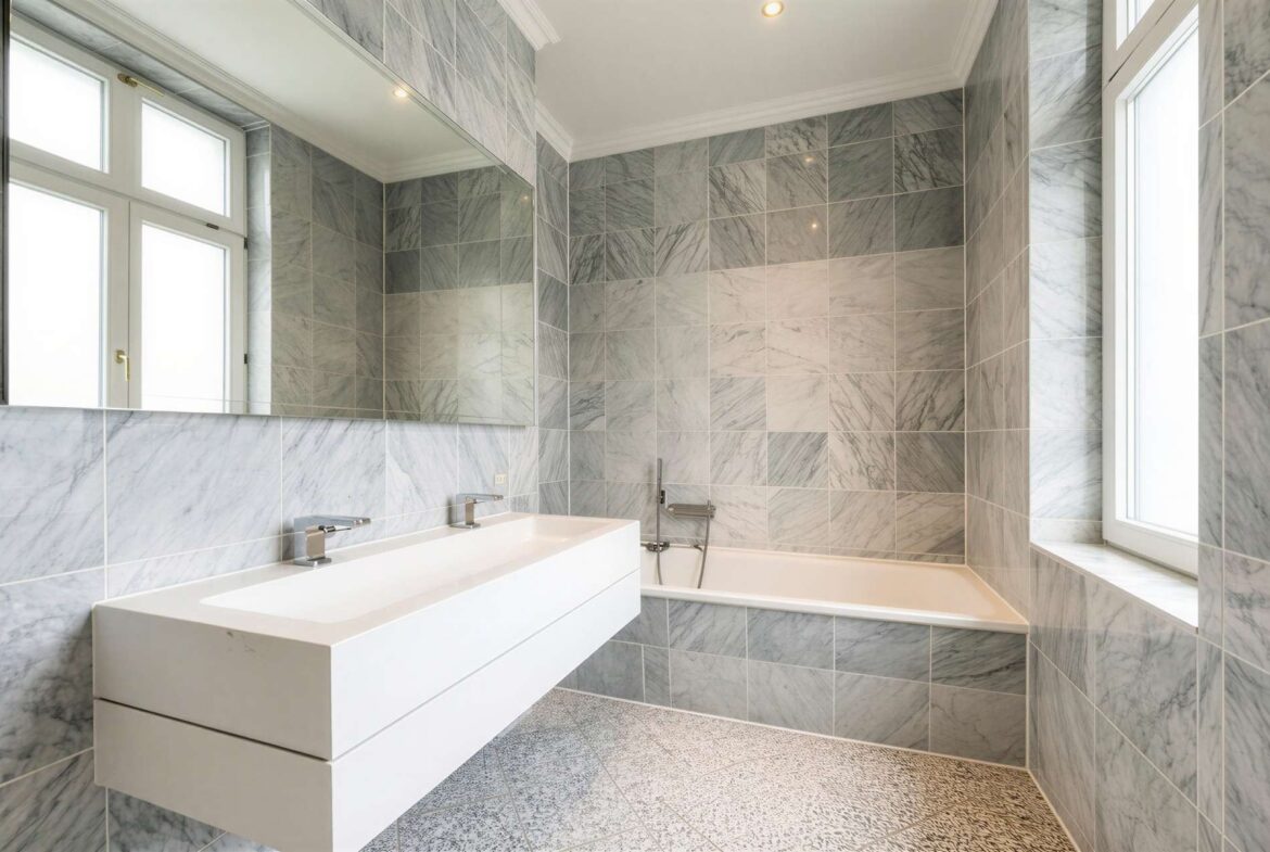 Marble-tiled bathroom with a white wall-mounted vanity and a built-in bathtub under a large window.