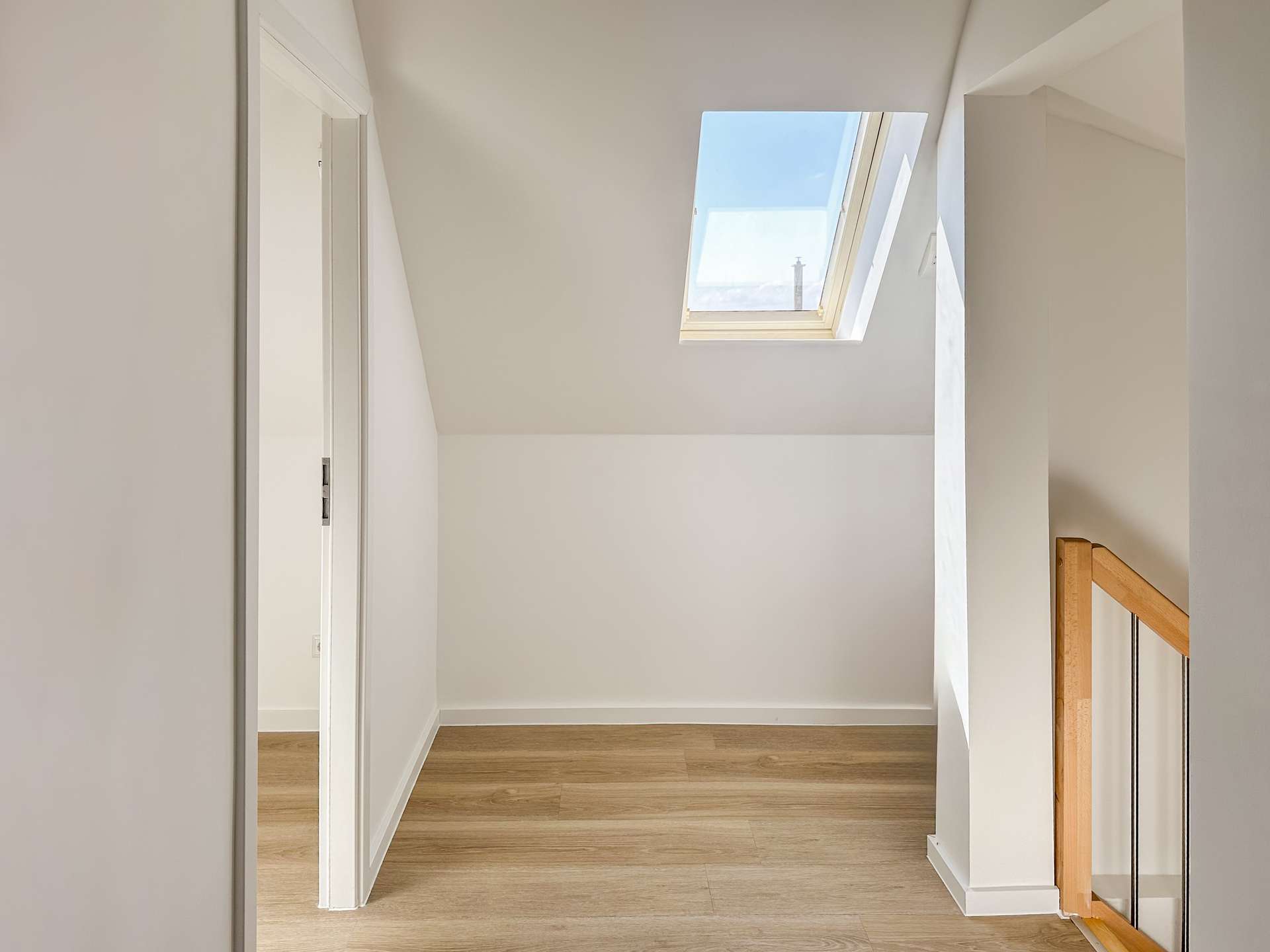 Bright upstairs hallway with an angled ceiling and a large skylight letting in daylight, white walls and a wooden handrail.
