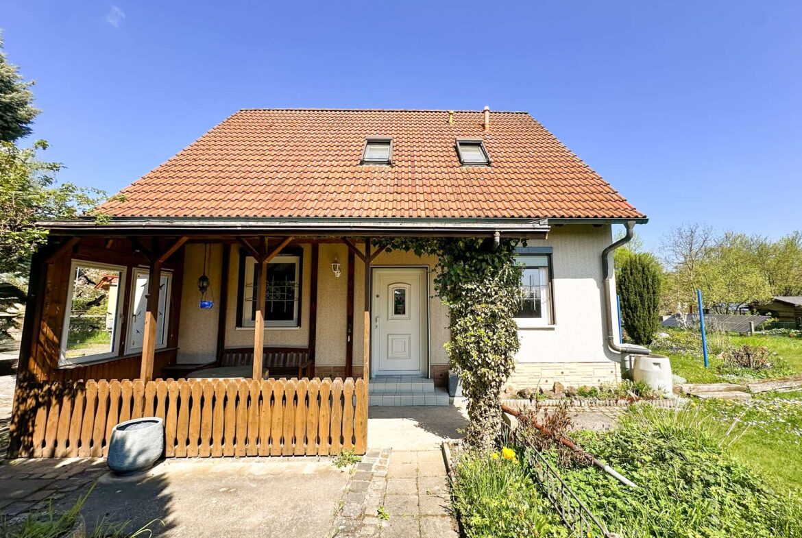 Front view of a beige house with a red tile roof and two dormer windows under a clear blue sky.