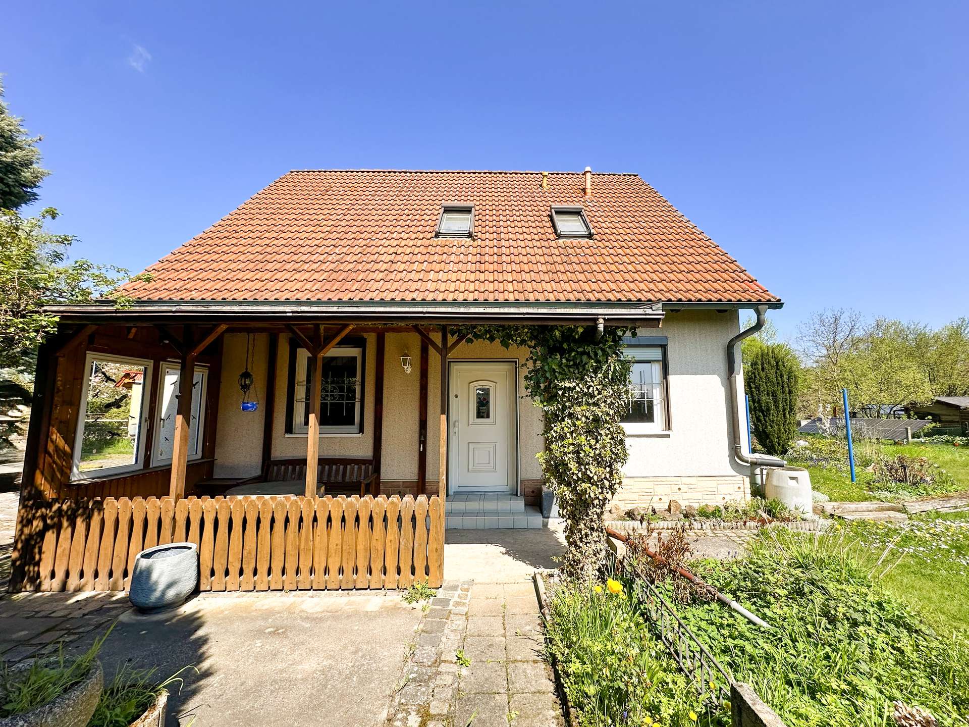Front view of a beige house with a red tile roof and two dormer windows under a clear blue sky.