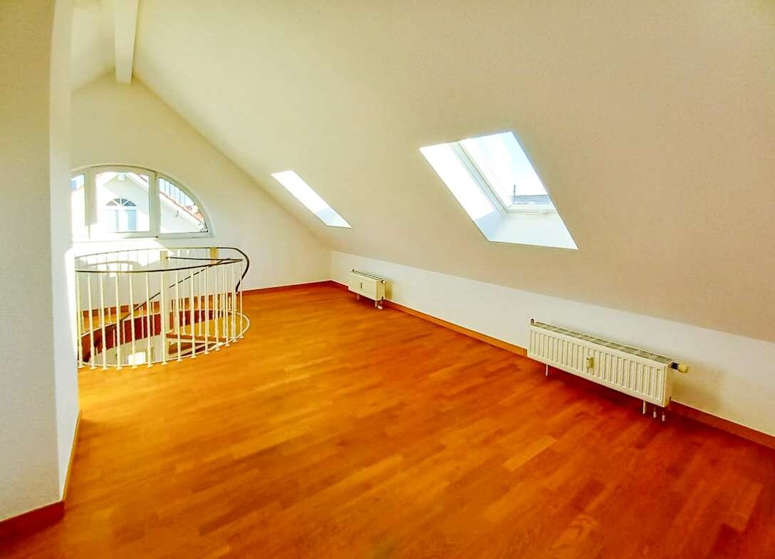 Bright attic loft with a sloped ceiling, two skylights, and a curved white railing beside the staircase.