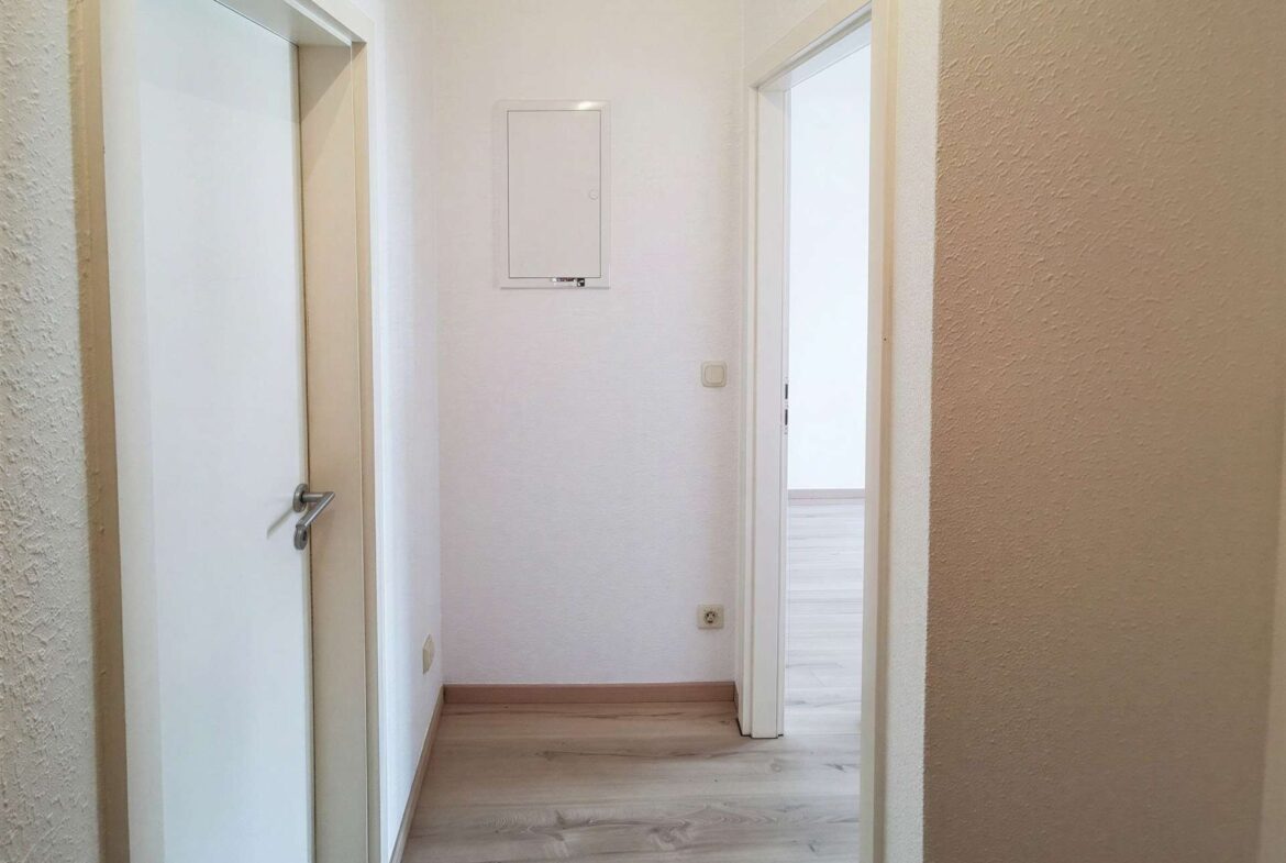 Narrow hallway with white doors on both sides, light wood flooring, and textured beige walls.