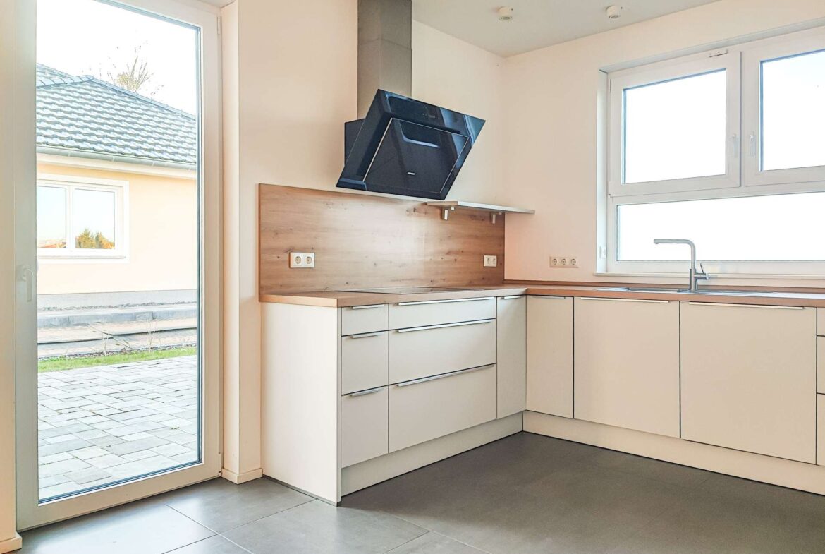 Modern L-shaped kitchen with white cabinets, wood countertops, and a black angled chimney hood.