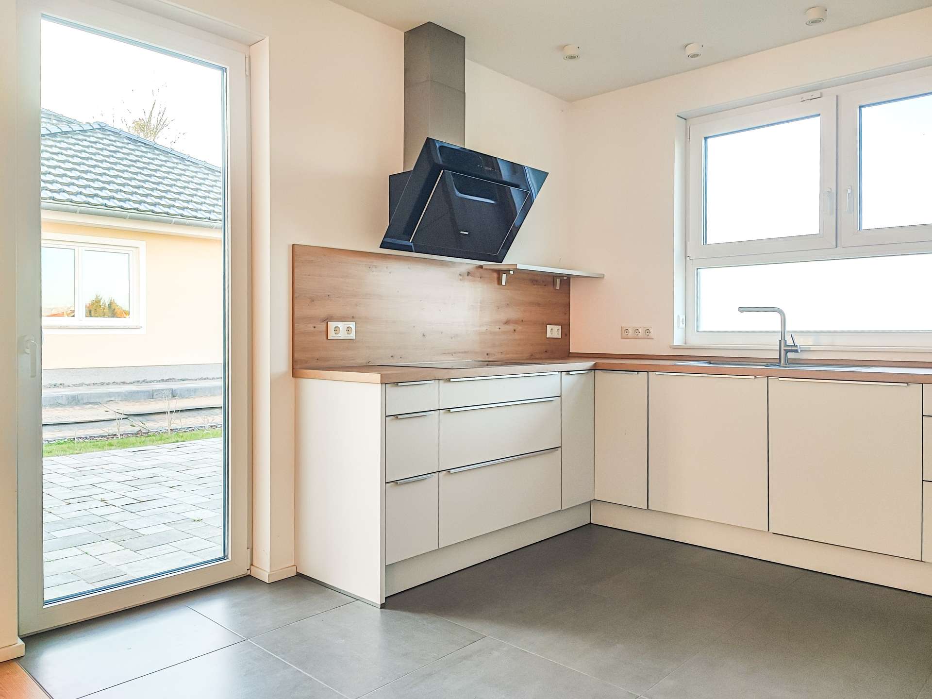 Modern L-shaped kitchen with white cabinets, wood countertops, and a black angled chimney hood.