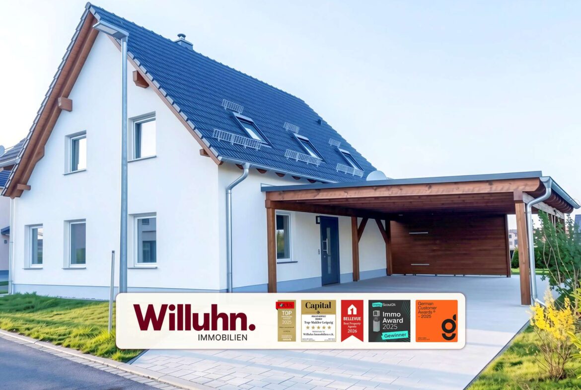 Modern white two-story house with a blue tiled pitched roof and a wooden-carport, branding for Willuhn Immobilien on a banner in the foreground.