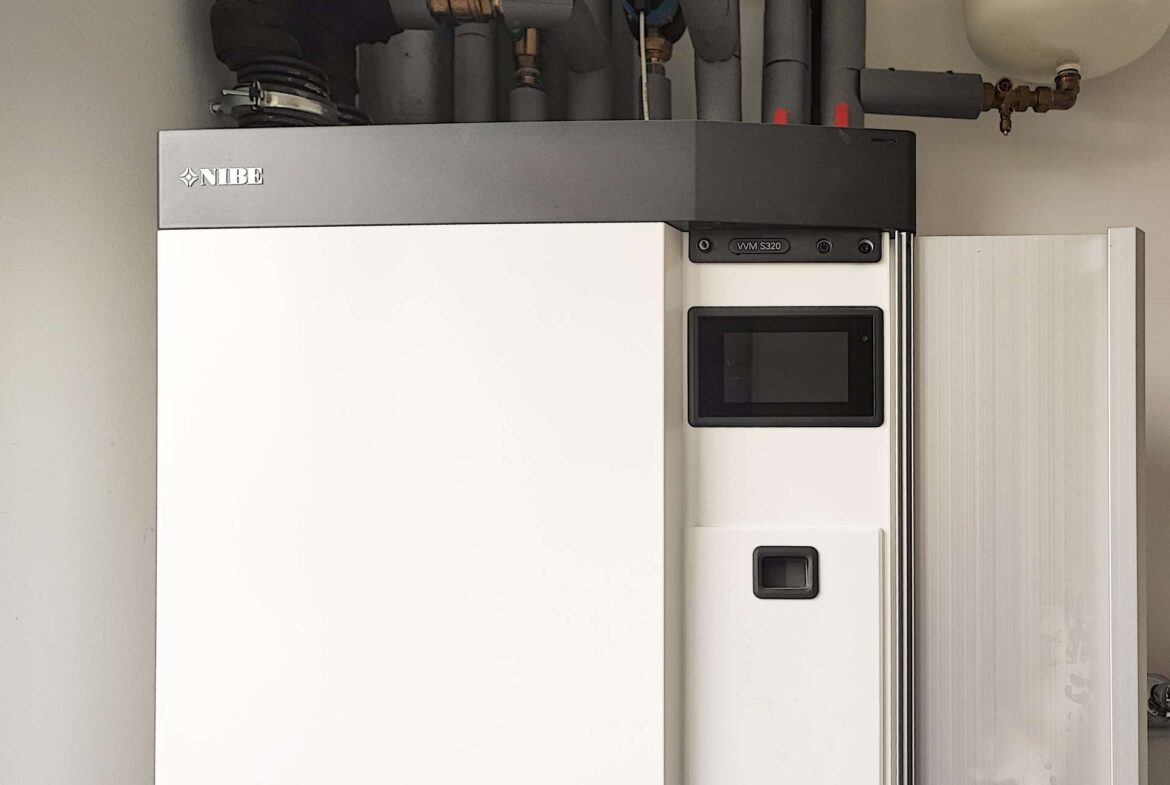 NIBE heat pump unit with a touchscreen control panel and overhead piping in a utility room