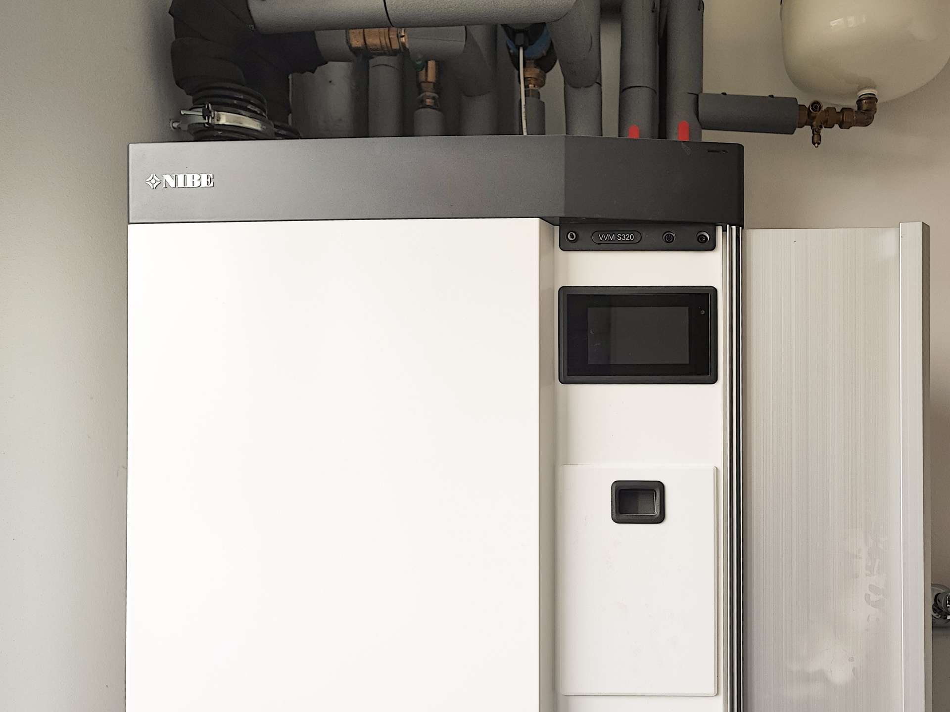 NIBE heat pump unit with a touchscreen control panel and overhead piping in a utility room