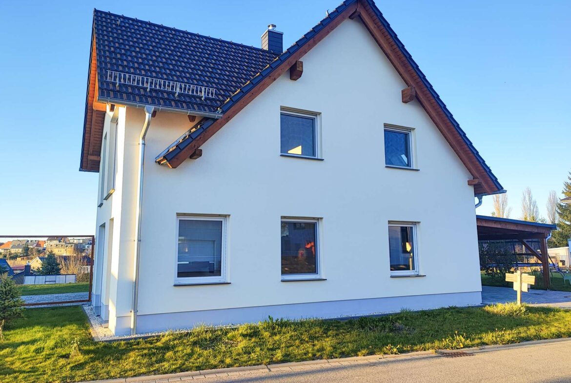 Front view of a white two-story house with a dark blue tiled pitched roof under a clear blue sky, sunny day.