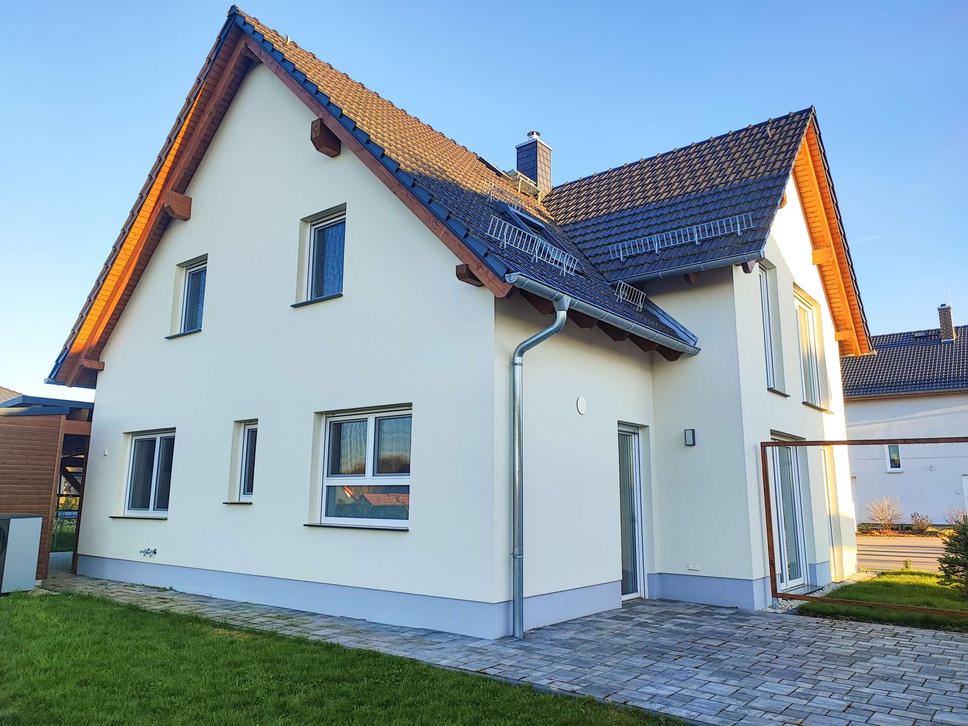 Modern white two-story house with blue trim, steep gabled roof, and a paved patio area in front.