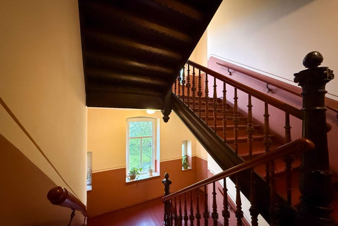 Wooden staircase with ornate balusters and a dark handrail in a warmly lit stairwell.