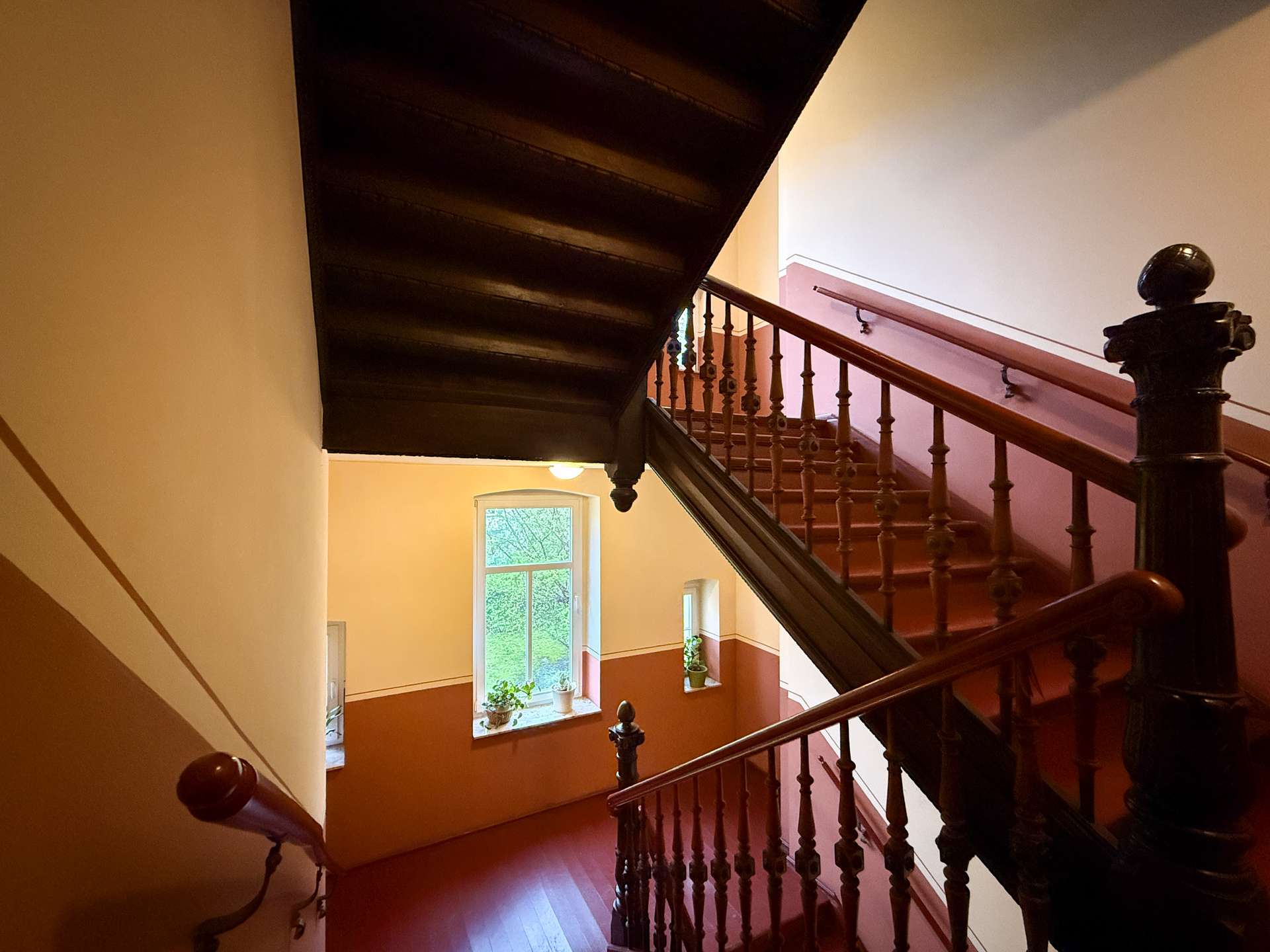 Wooden staircase with ornate balusters and a dark handrail in a warmly lit stairwell.