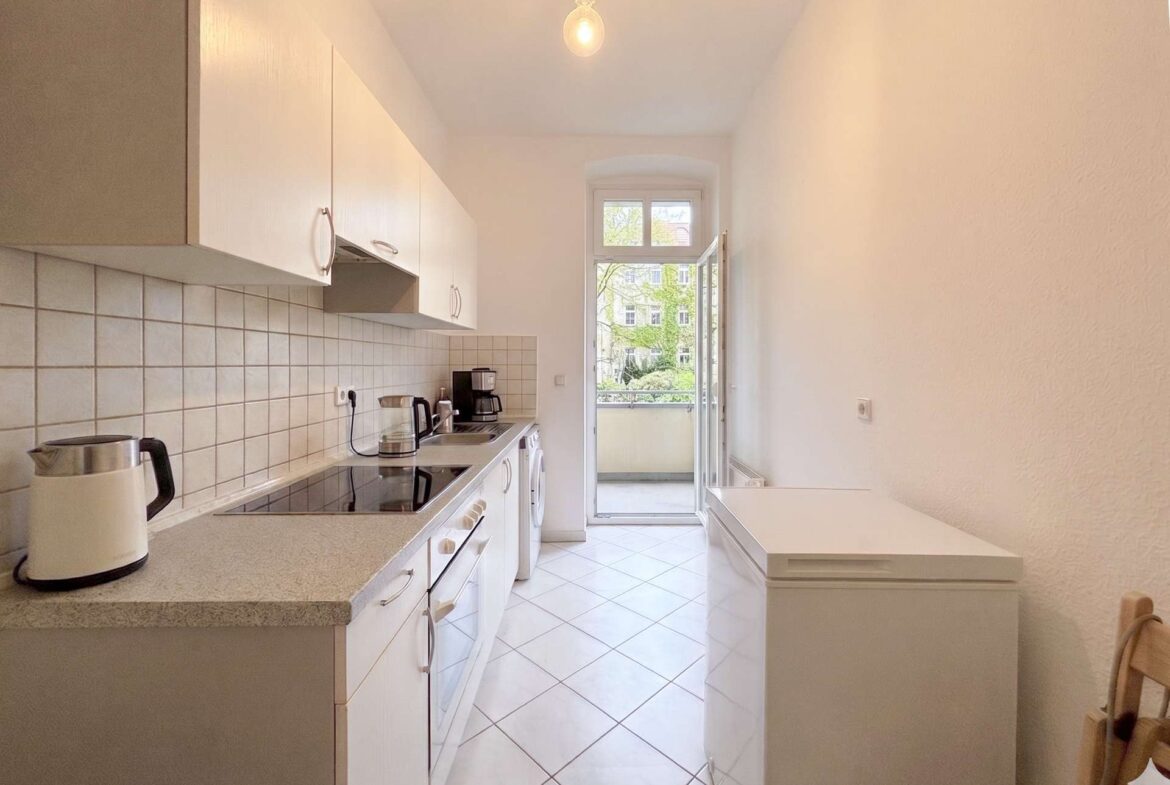 Bright narrow kitchen with white cabinets, tiled backsplash, and a balcony door at the far end.