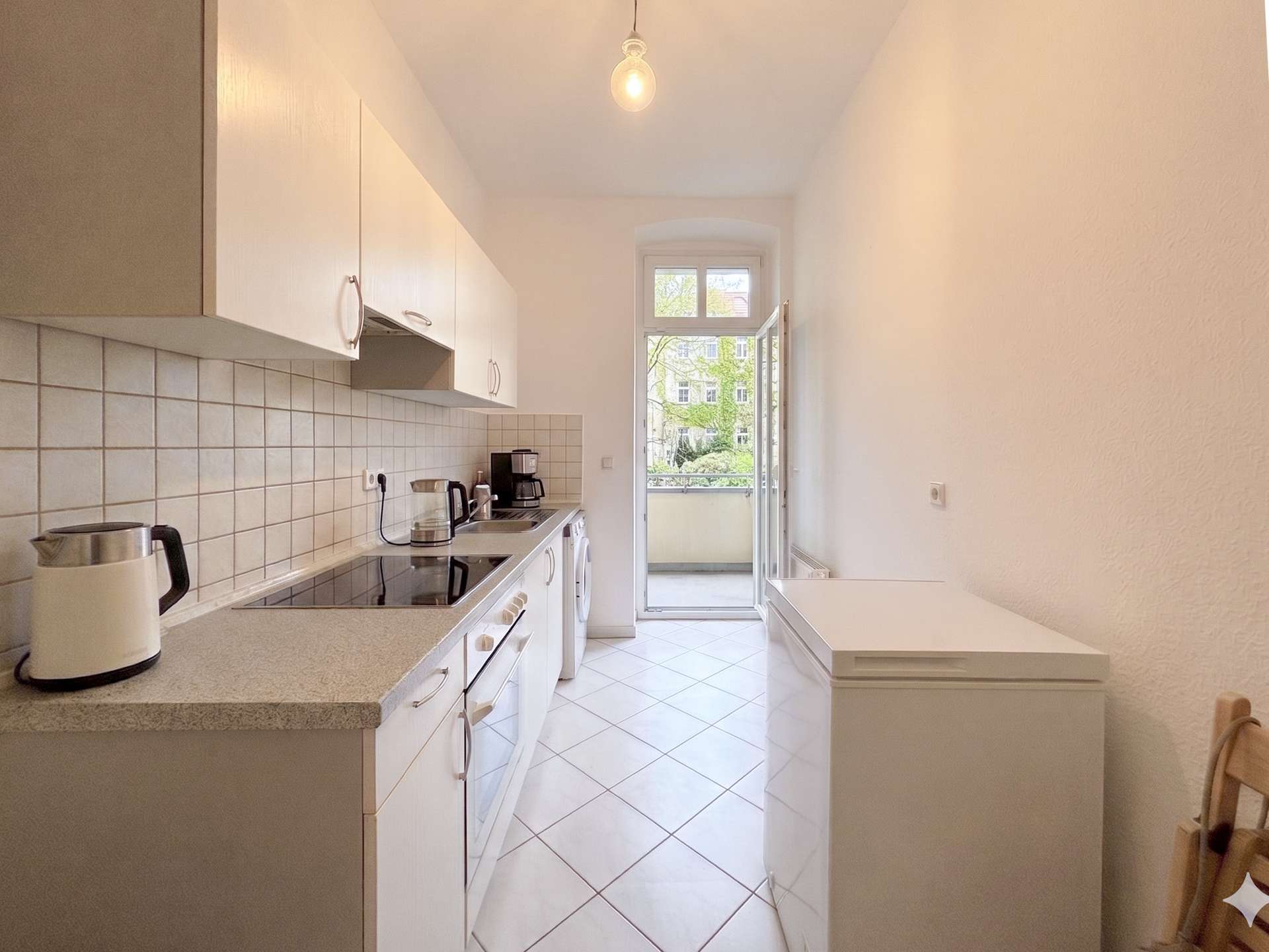 Bright narrow kitchen with white cabinets, tiled backsplash, and a balcony door at the far end.