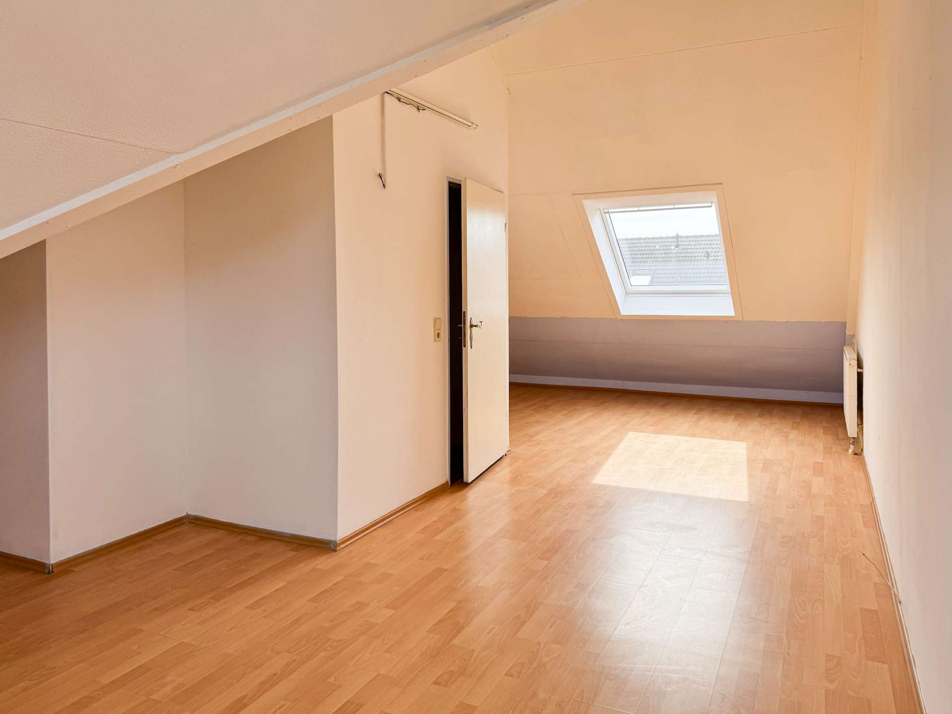 Sunlit empty attic room with a slanted ceiling, skylight window, and light wood floor.