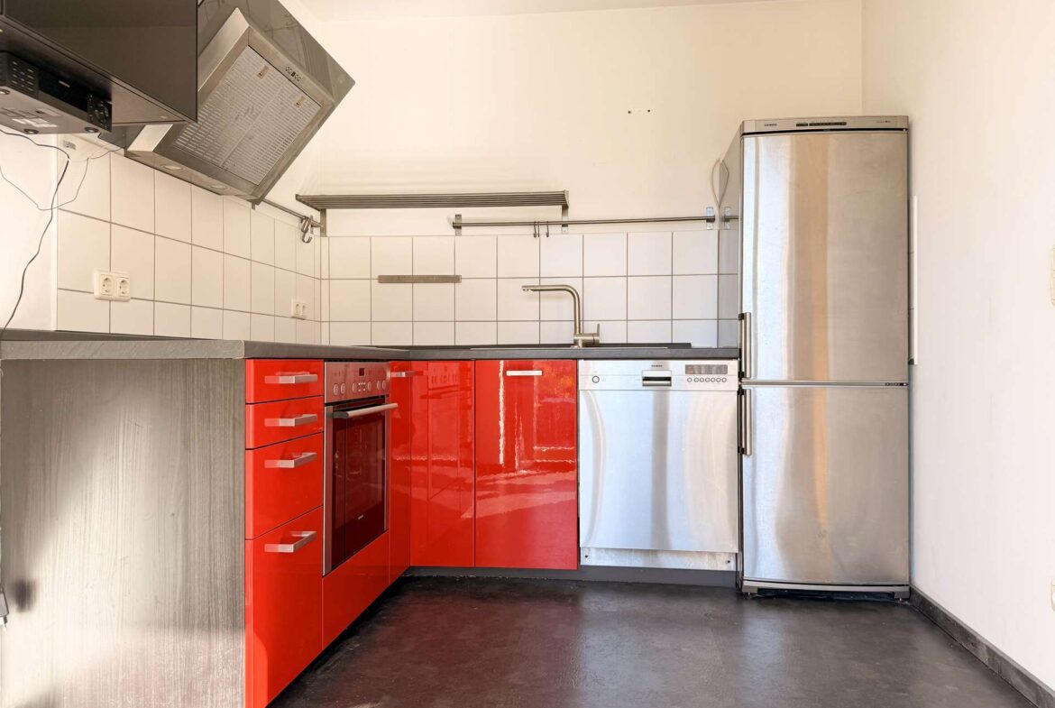 Compact kitchen with glossy red cabinets, stainless oven, and a tall silver refrigerator against a white-tiled backsplash.